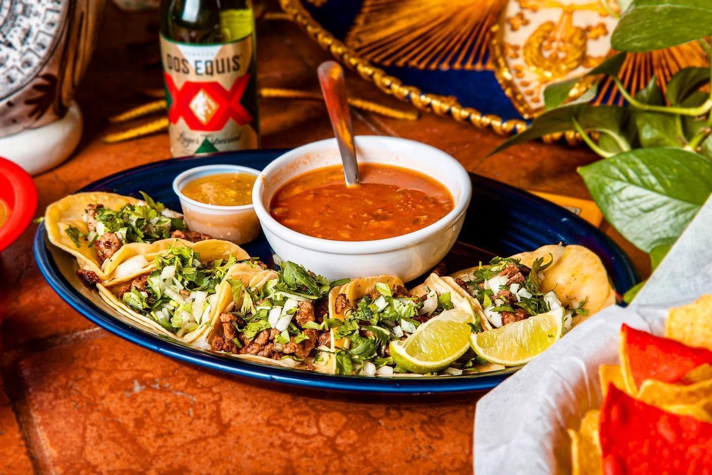 Mexican platter with tacos and salsa bowls on a blue plate, served with a beer bottle and tortilla chips