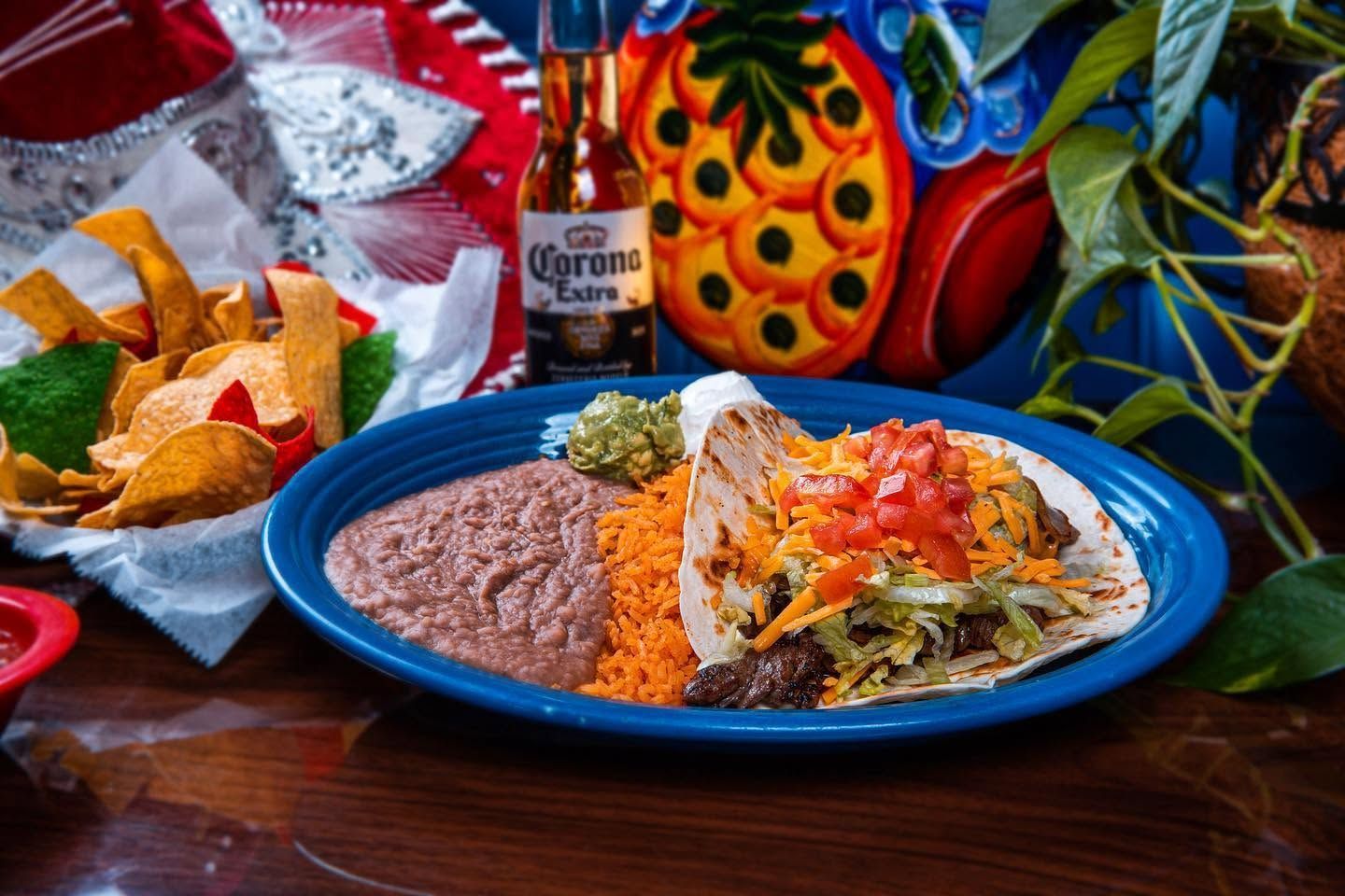 Mexican meal with tacos, refried beans, chips, and a Corona bottle on a colorful table