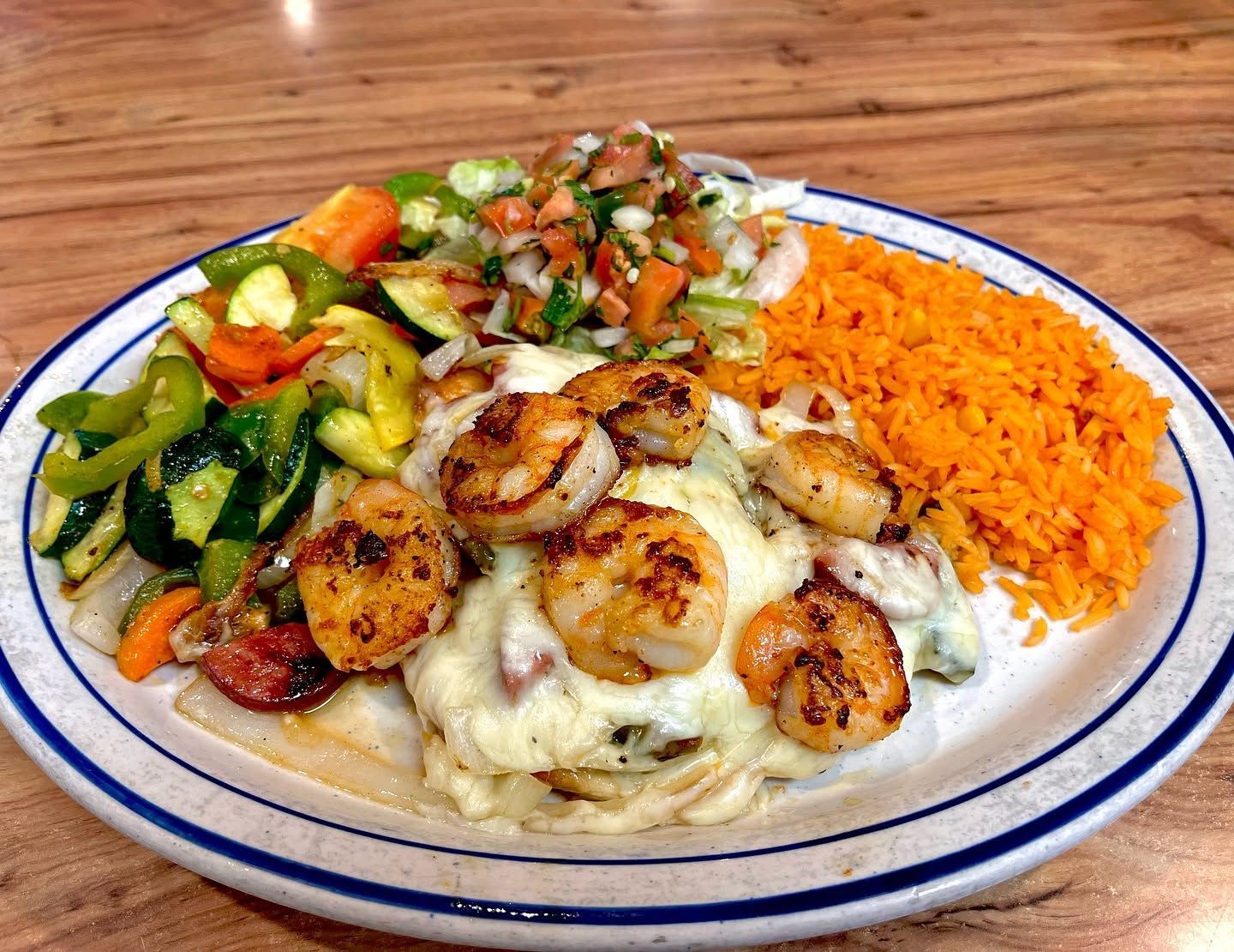Plate of shrimp in creamy sauce with rice, sautéed vegetables, and diced tomato relish