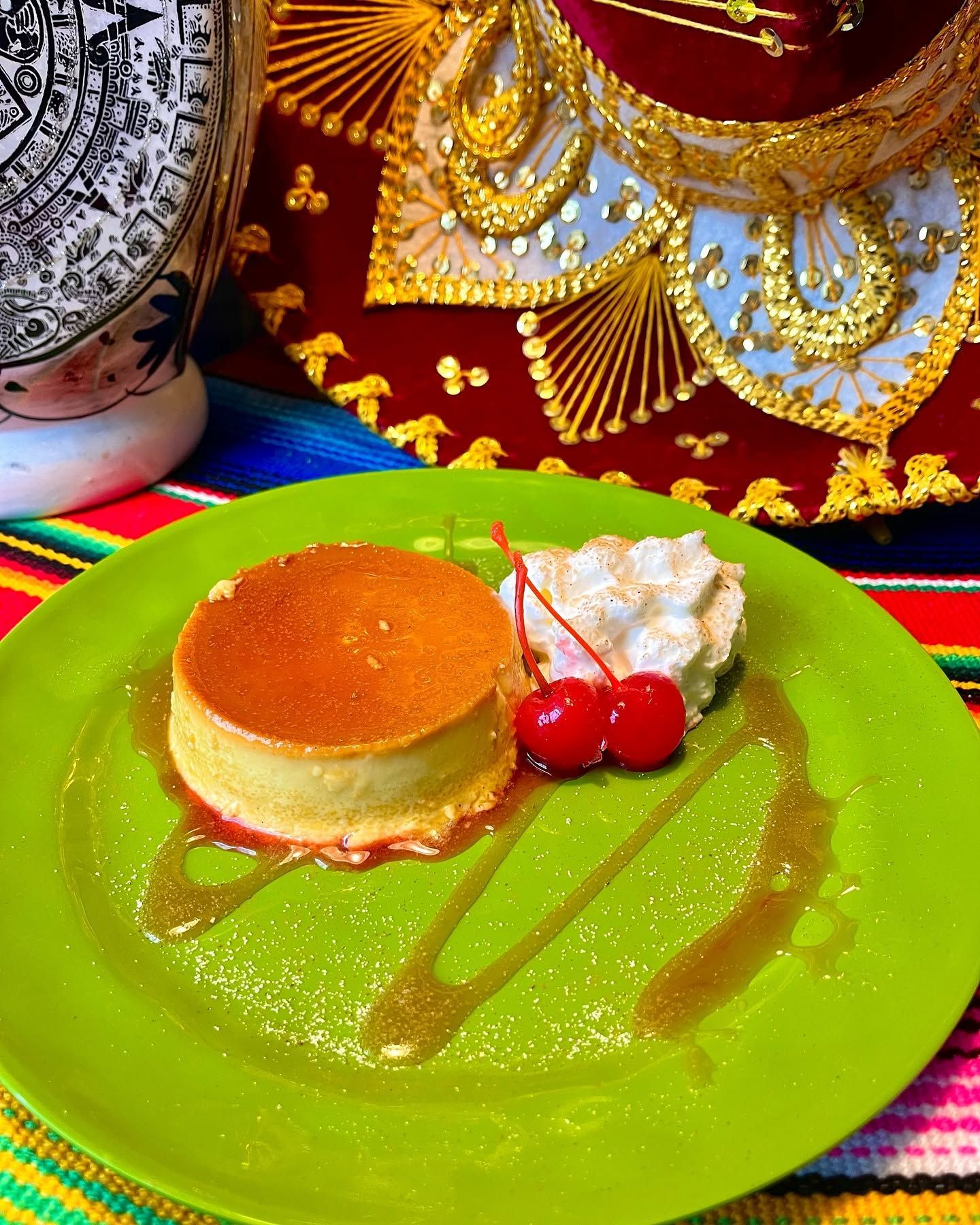 Green plate with caramel flan, whipped cream, and cherries on a festive cloth