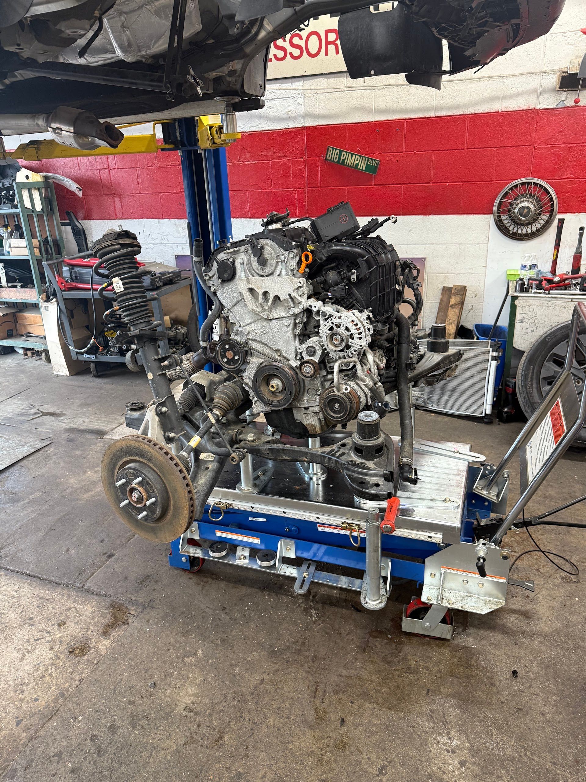 Engine on a blue shop cart being repaired in an auto garage with a car lifted overhead. | A & Z Auto Repair
