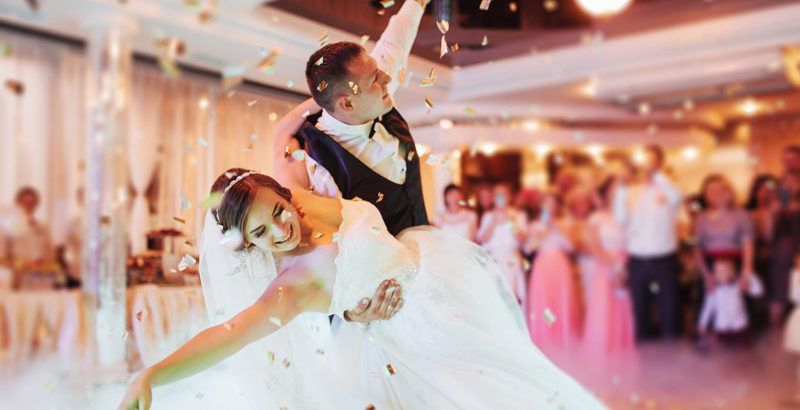 Noivos dançando, confete caindo. Cenário da recepção do casamento, expressões alegres.