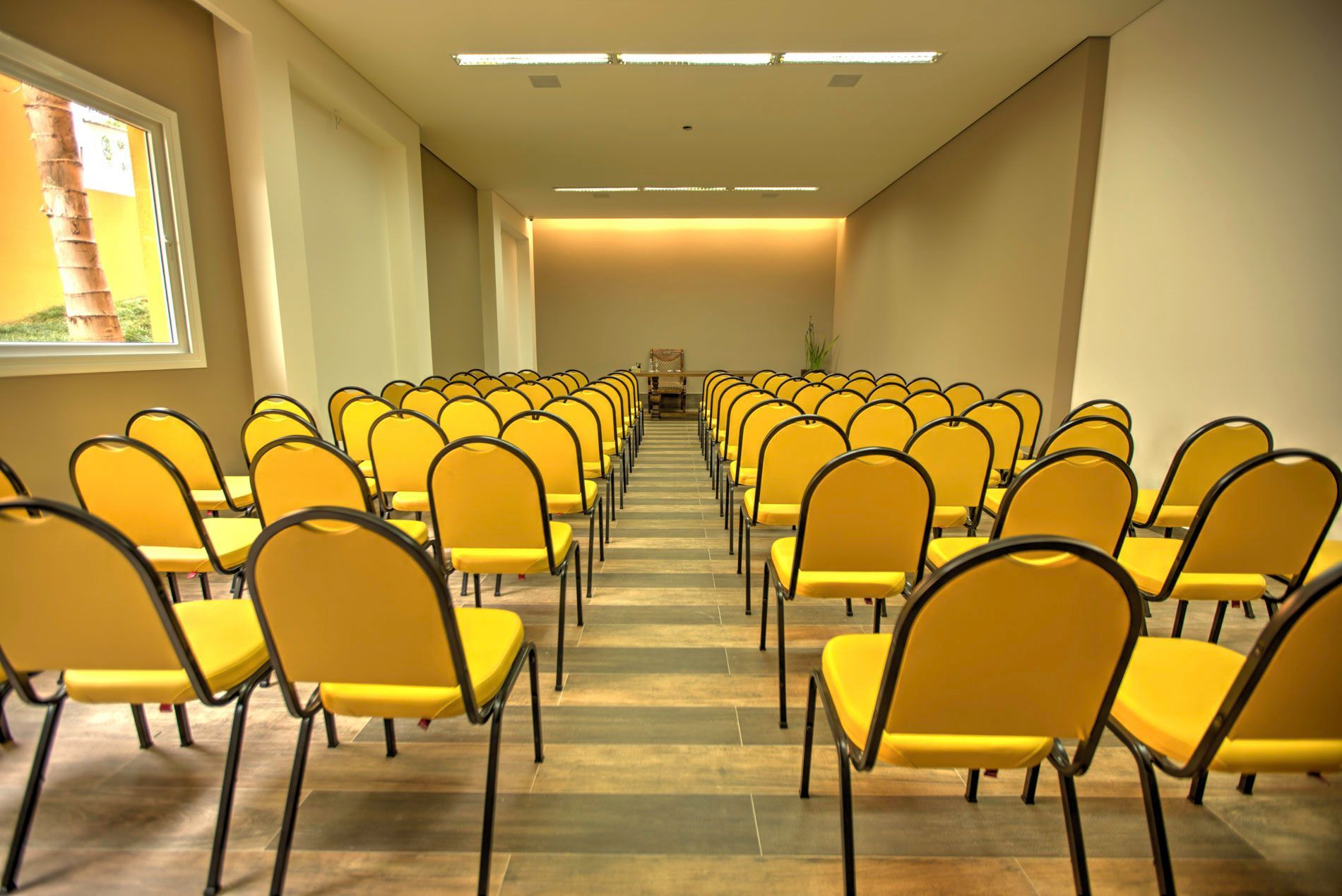Fileiras de cadeiras amarelas em uma sala de reuniões com paredes de cores claras.