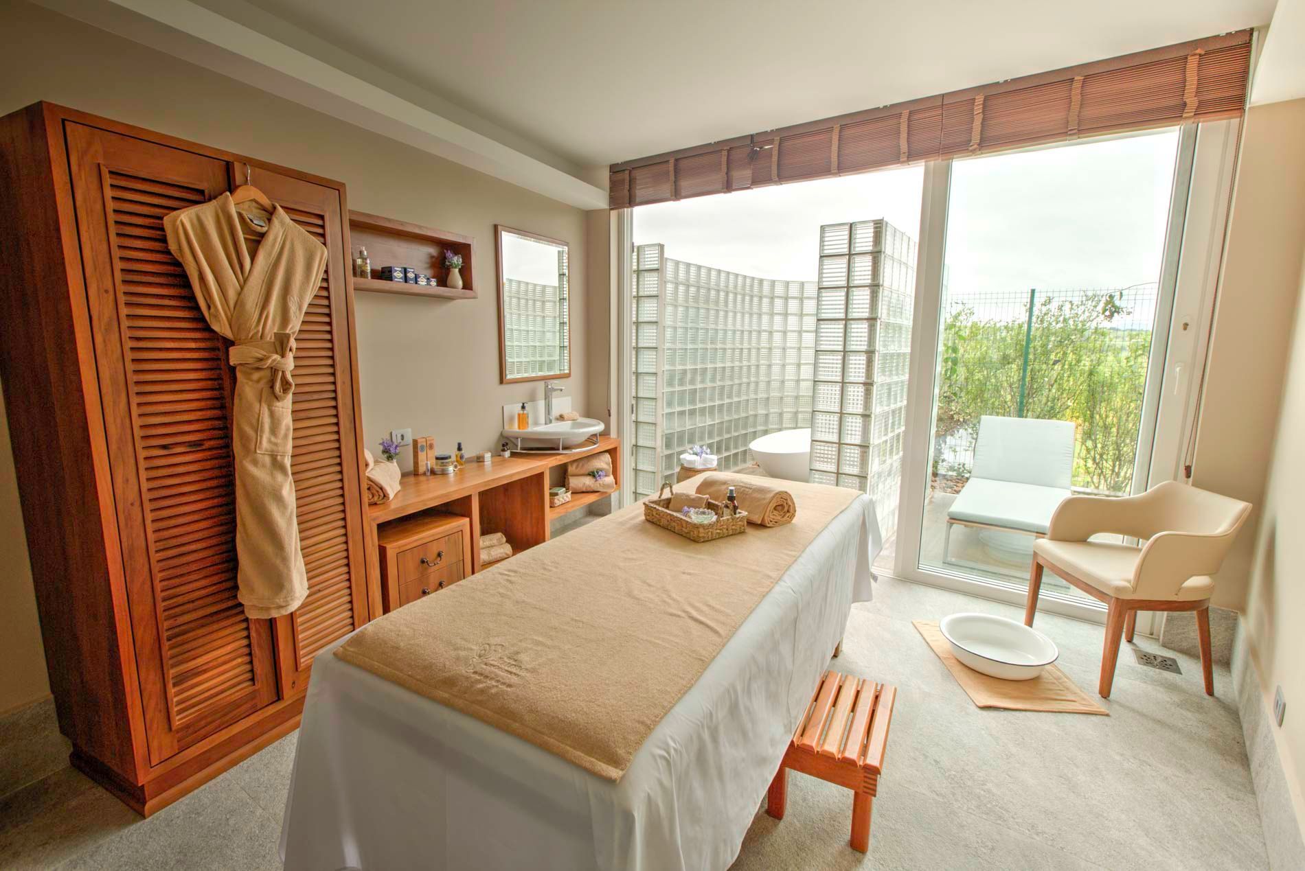 Sala de spa com mesa de massagem, roupão e assentos ao ar livre.