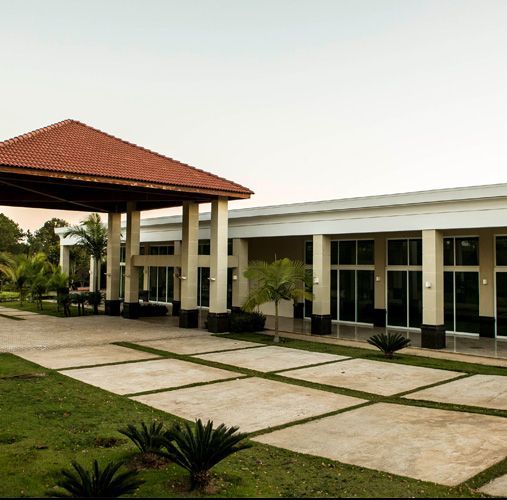 Um edifício moderno e branco com telhado de telhas vermelhas e grandes janelas, cercado por grama verde