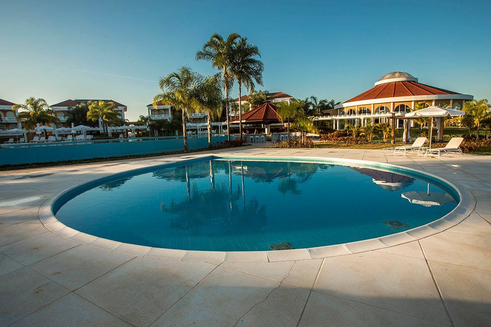 Piscina com palmeiras e edifícios do resort sob um céu azul.