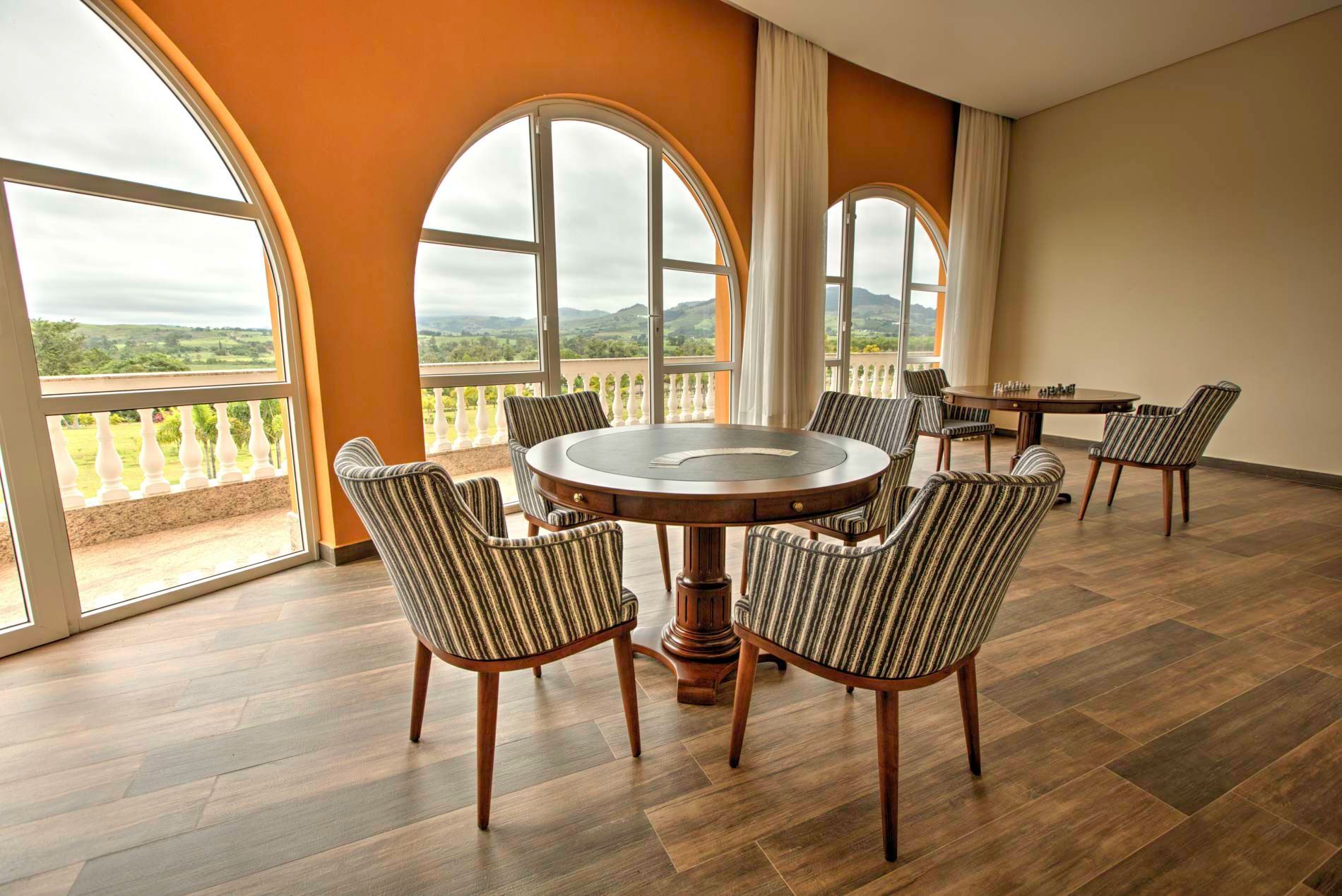 Sala com mesa redonda, cadeiras estampadas, janelas em arco e vista para a paisagem.