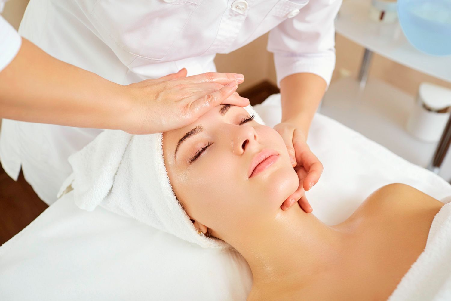 Mulher recebendo uma massagem facial em um spa, olhos fechados, mãos tocando suavemente seu rosto.