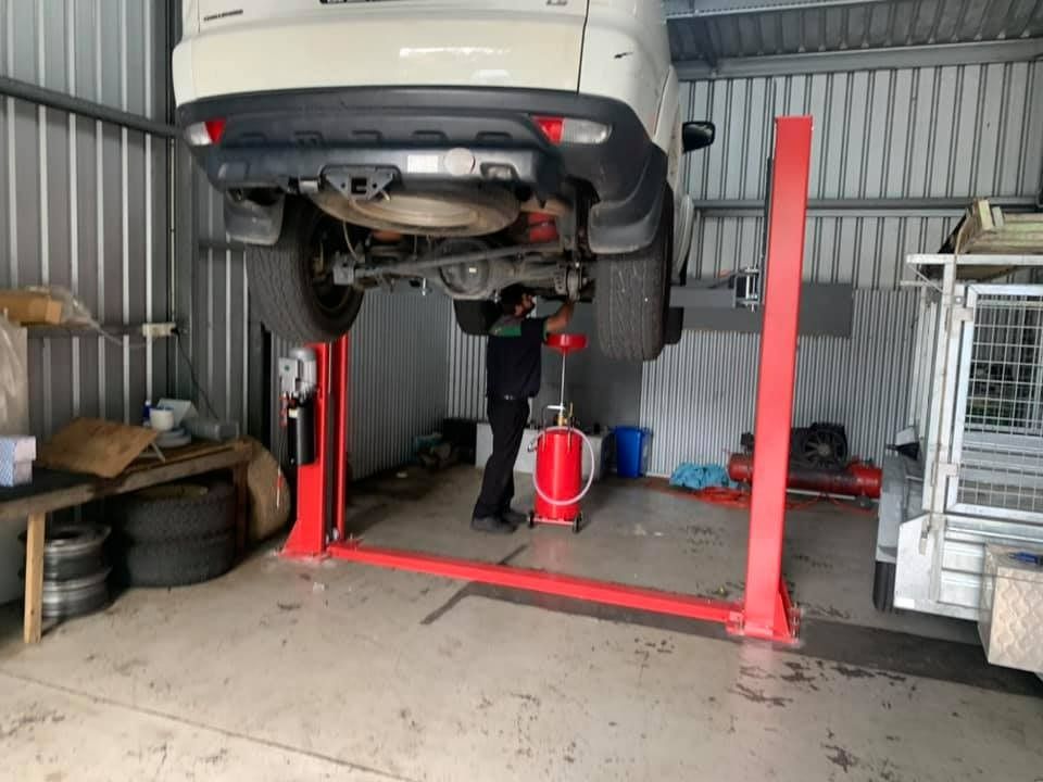 Car Raised on a Red Lift in a Garage, a Mechanic Working Underneath — Adam's Automotive Centre in Nambour, QLD