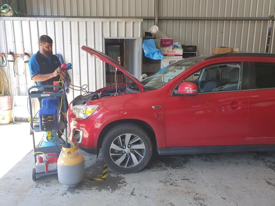 Mechanic servicing red SUV's AC with diagnostic equipment in a garage. — Adam's Automotive Centre in Nambour, QLD