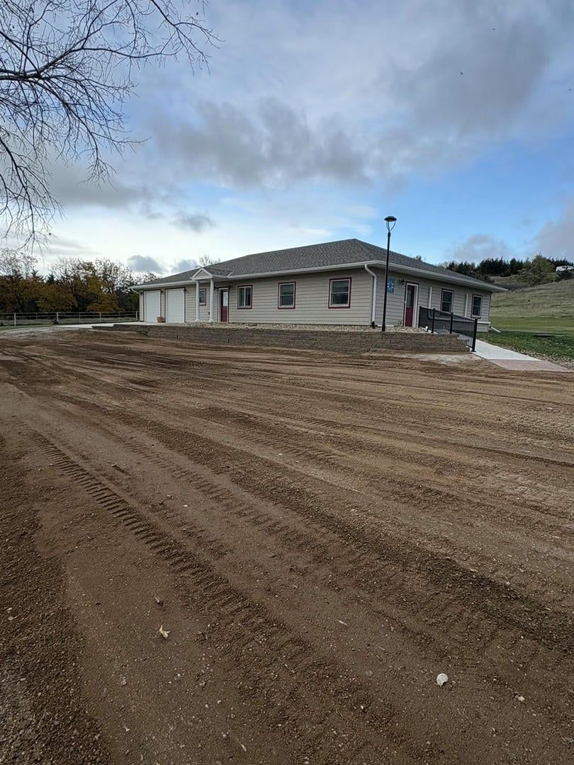 A one-story house with a gravel driveway against a cloudy sky.