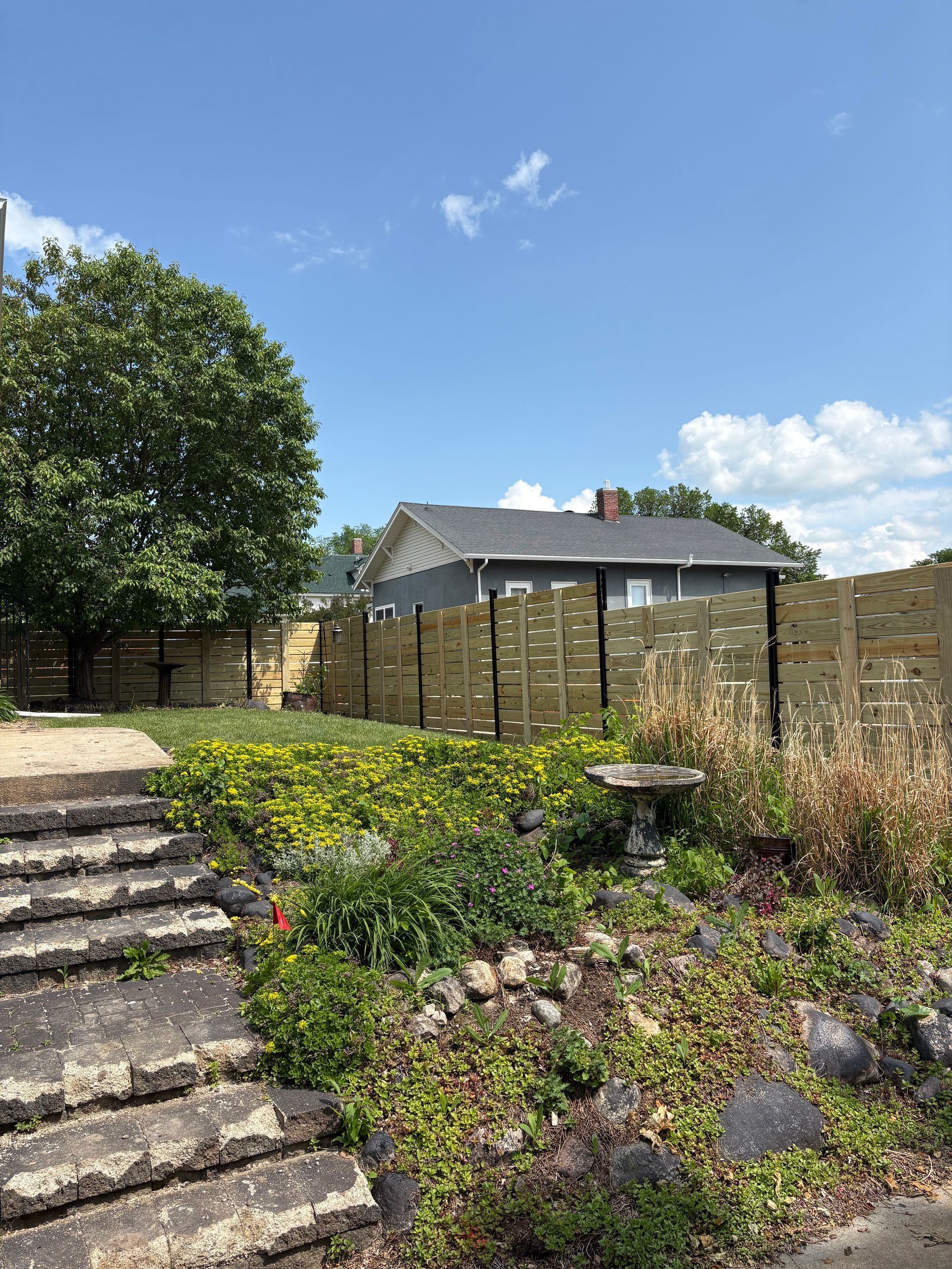 Backyard with newly built wooden fence, stairs, and greenery under a blue sky.