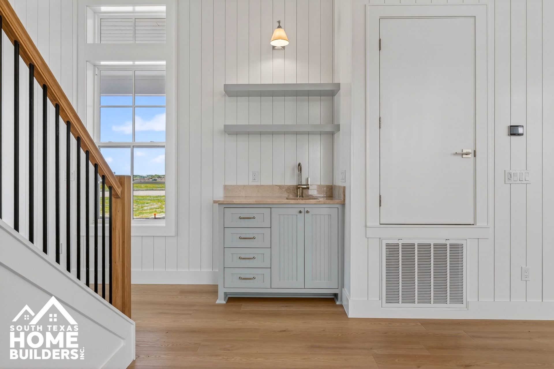 Bright entryway with staircase, gray cabinet, white door, and wood floors in a modern home interior