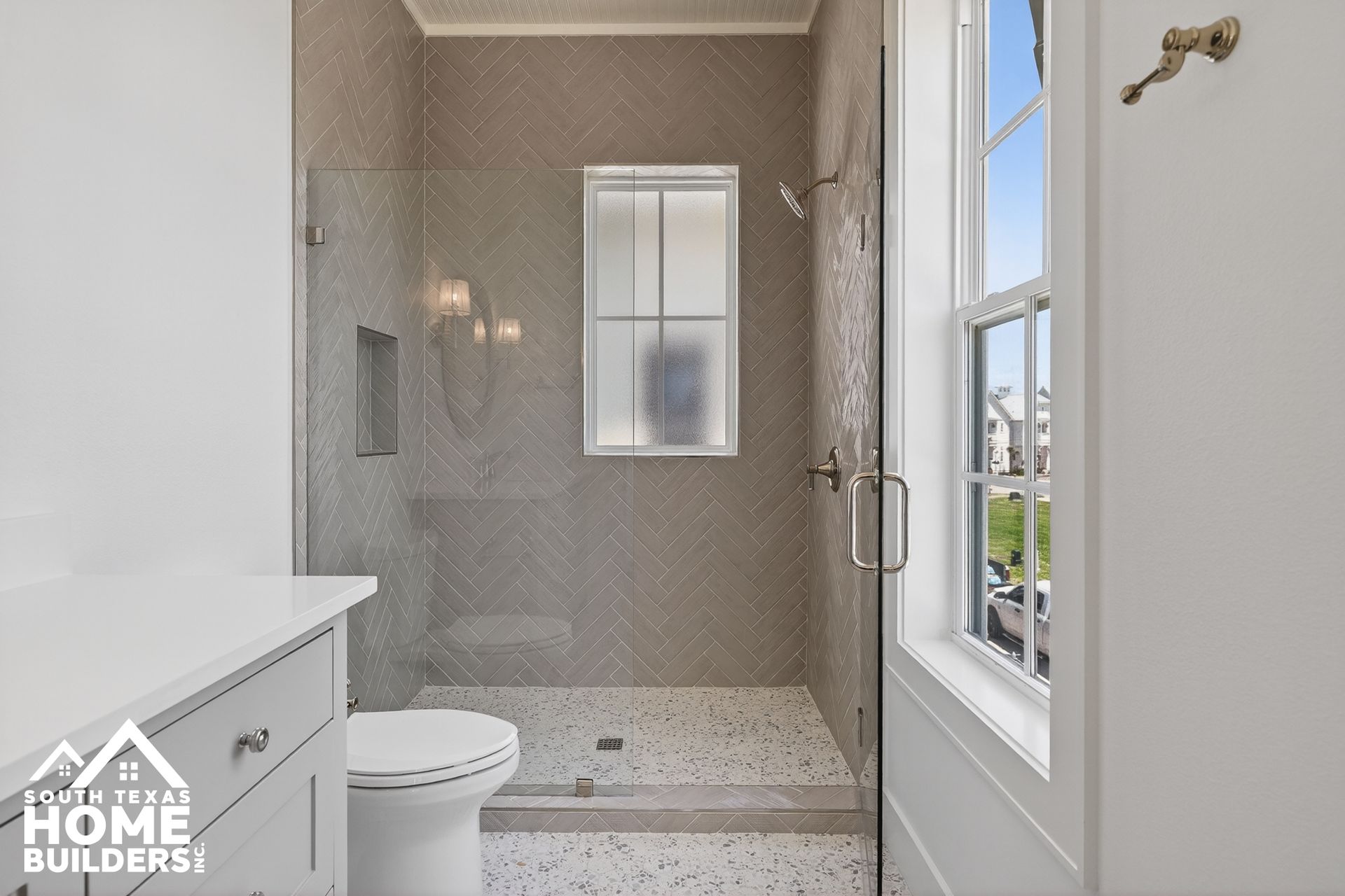 Modern bathroom with white vanity, toilet, glass shower, and gray tile walls