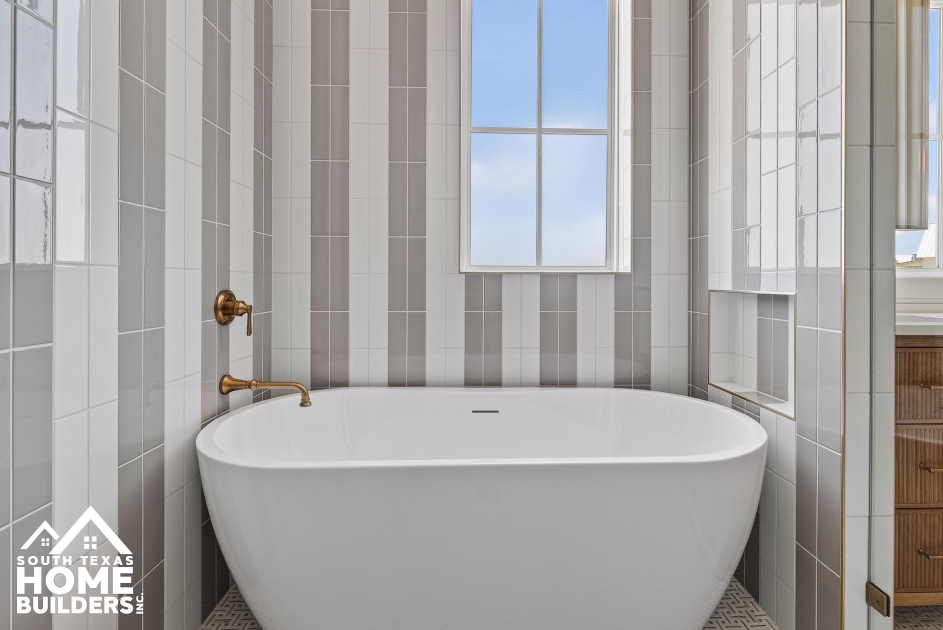 Modern bathroom with a white freestanding bathtub, brass fixtures, and gray tiled walls