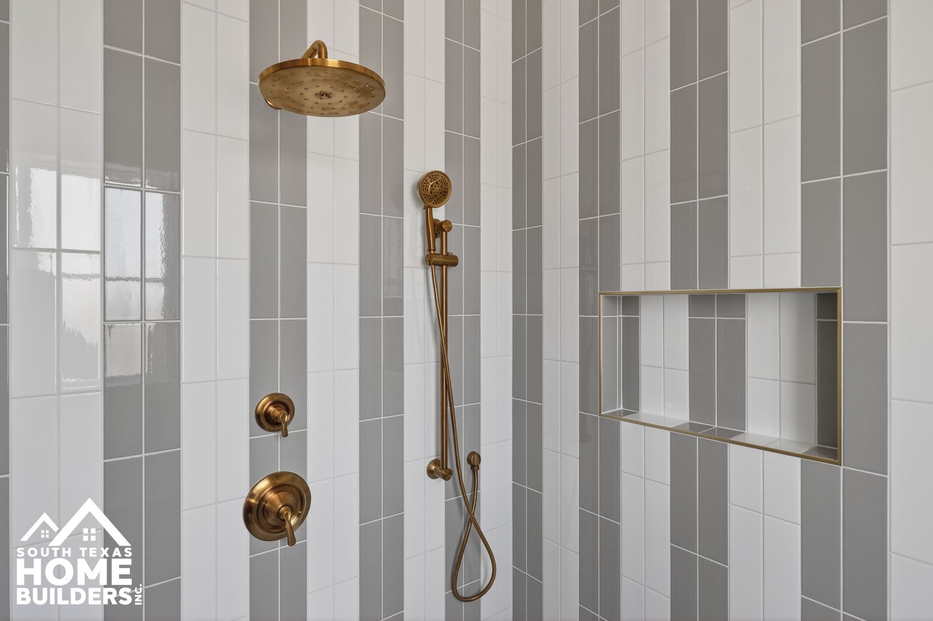 Modern shower with gray striped tile, gold fixtures, and built-in niche