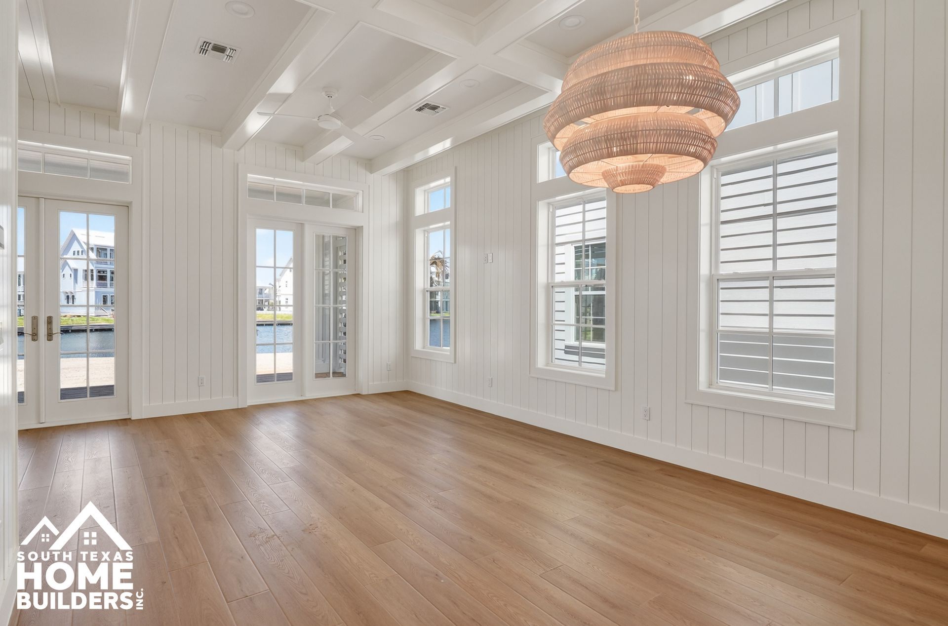 Bright empty living room with white walls, wood floors, tall windows, and a woven pendant light