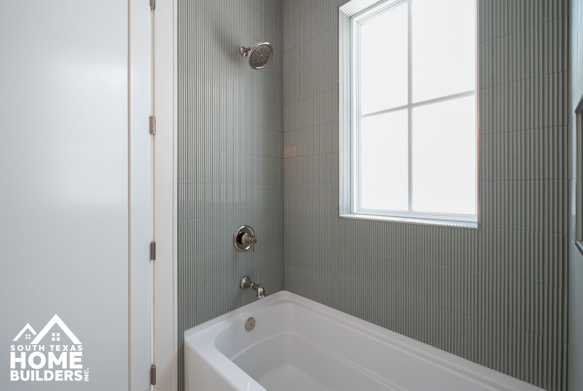 Modern bathroom with striped tile walls, white tub, and frosted window