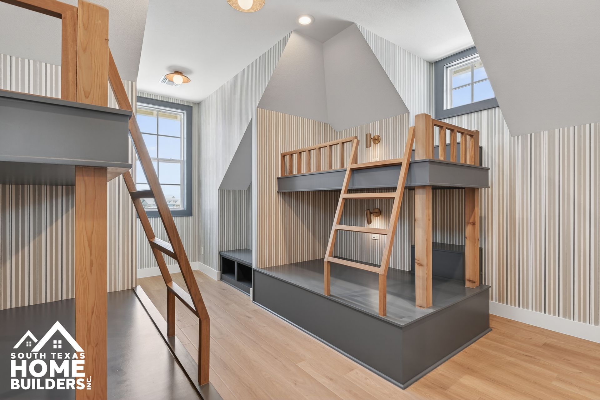 Modern loft-style bunk room with wood beds, ladder, skylights, and light wood flooring