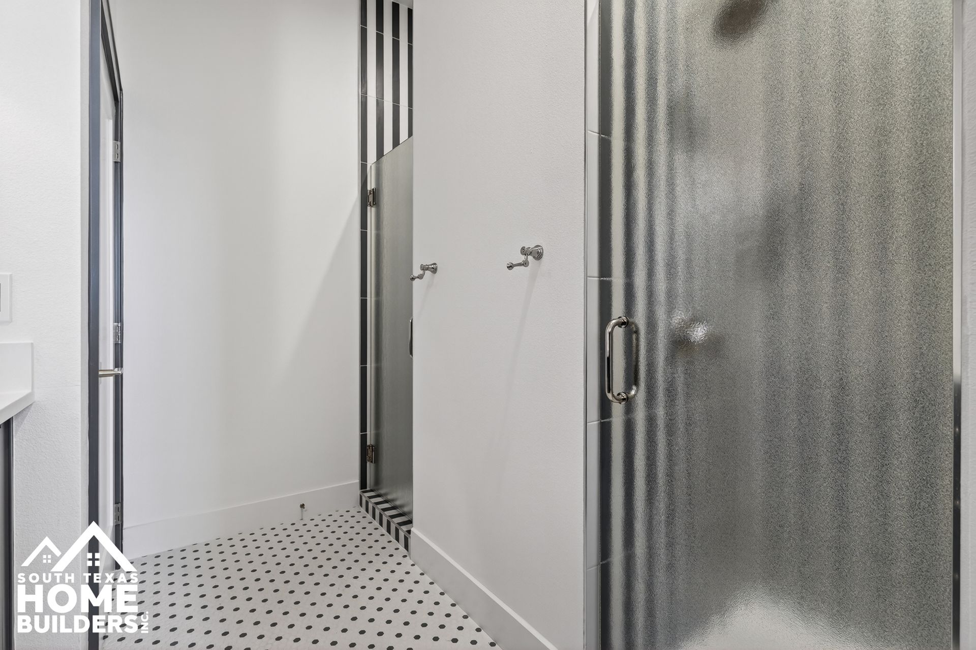 Modern bathroom with white walls, frosted glass shower door, and black-and-white tile floor