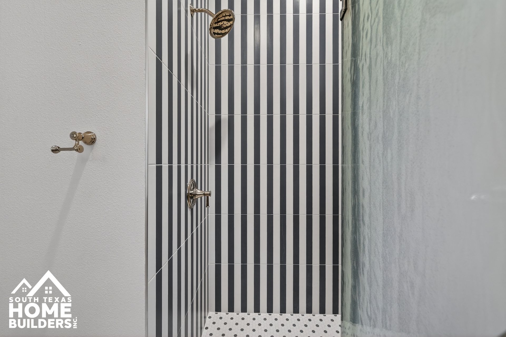 Striped glass shower enclosure with chrome fixtures in a tiled bathroom