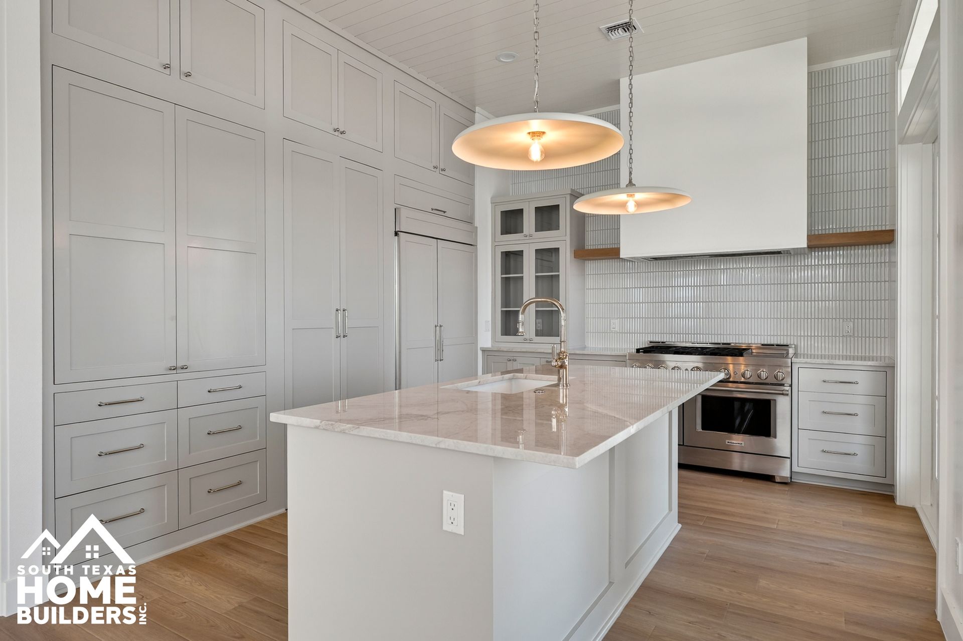 Bright modern kitchen with white cabinets, marble island, pendant lights, and wood floors