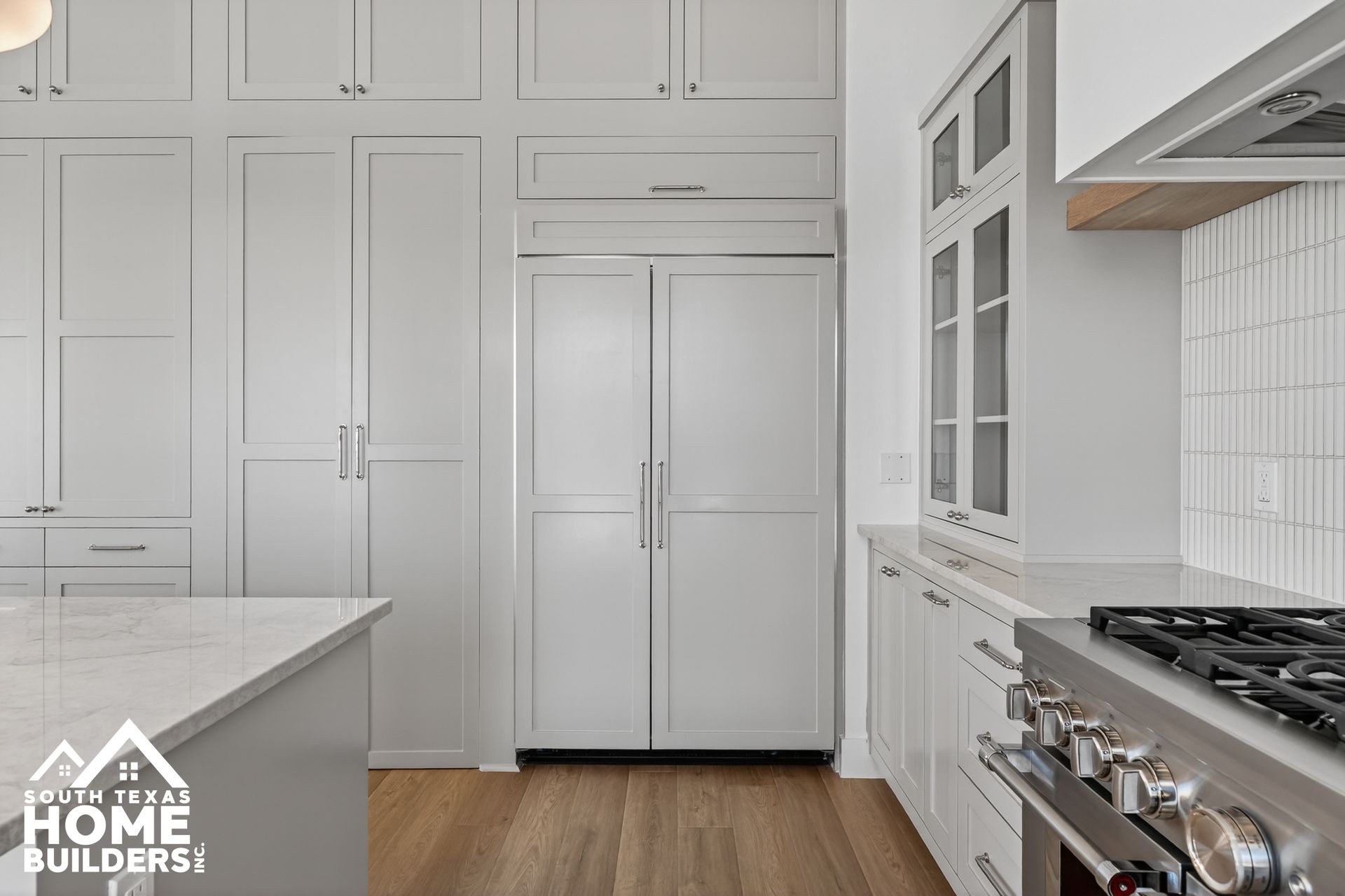 Modern white kitchen with built-in cabinets, stainless stove, and wood floors