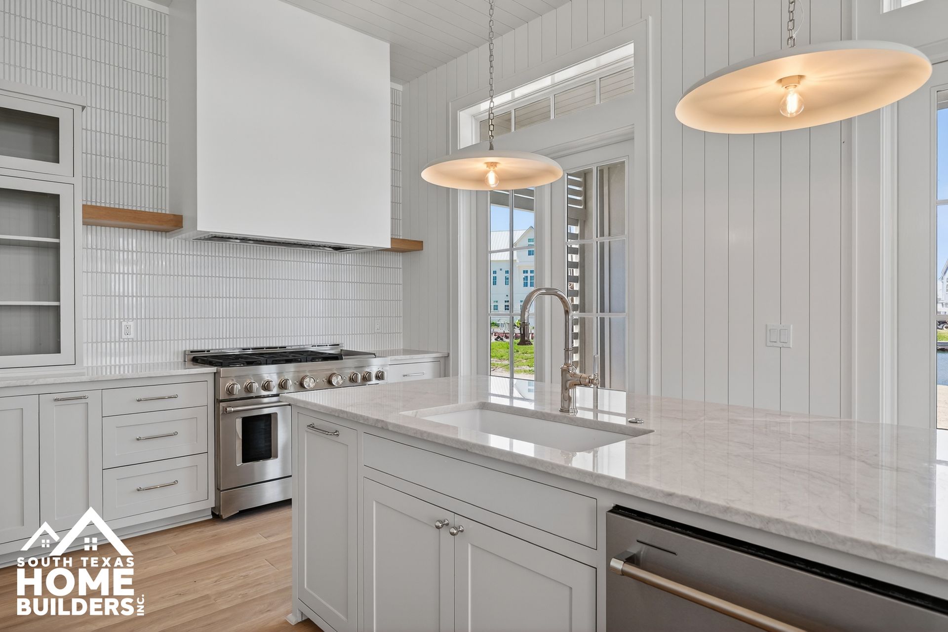 Bright white modern kitchen with island, pendant lights, and stainless steel appliances