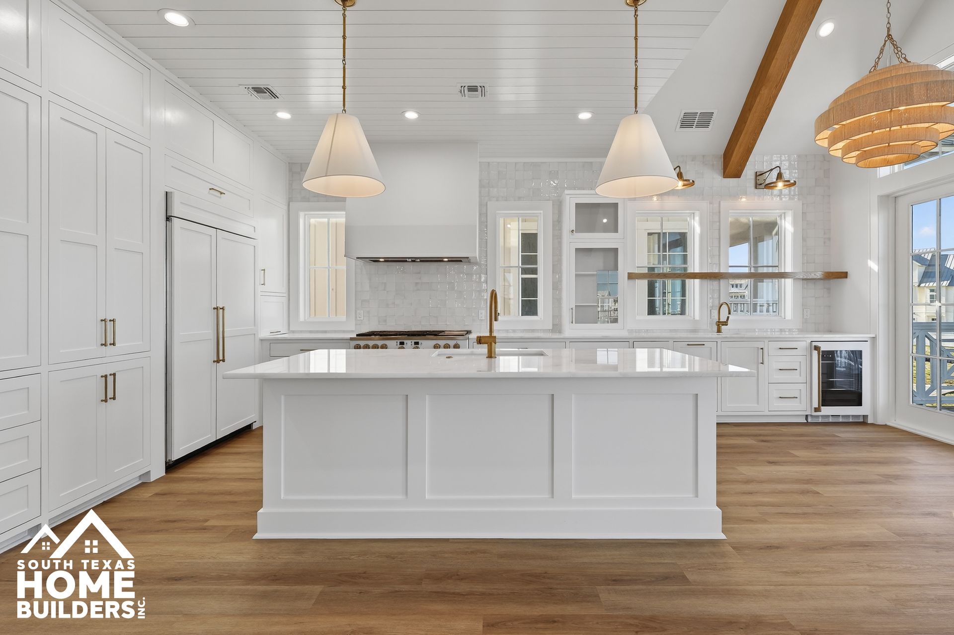 Bright white modern kitchen with island, pendant lights, wood floor, and large windows