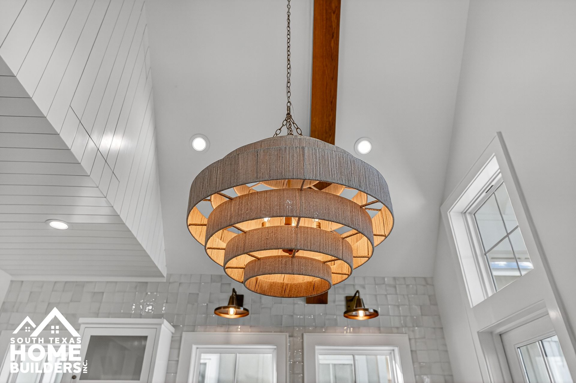 Large tiered wooden chandelier hanging in a bright white vaulted ceiling room