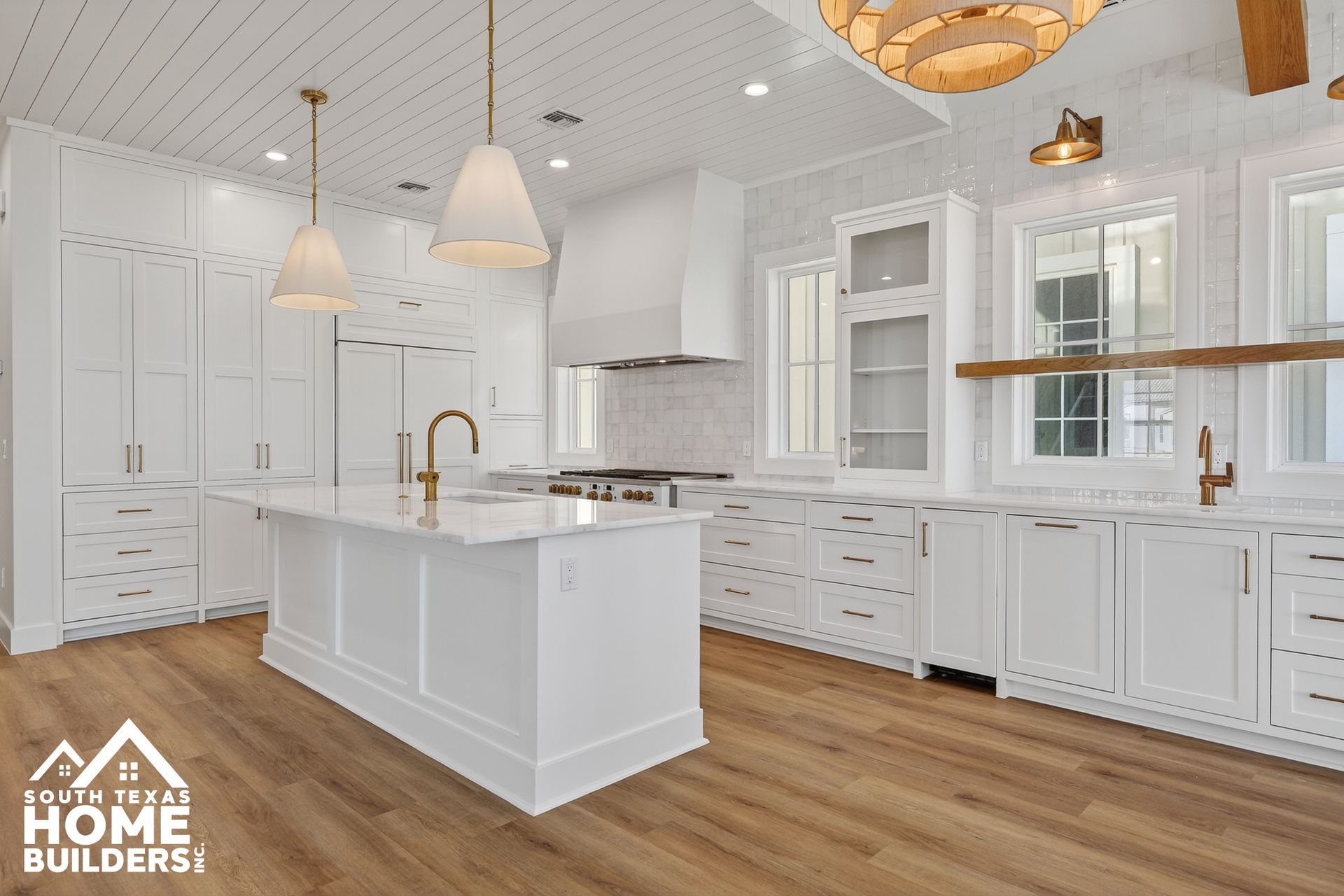 Bright white modern kitchen with island, brass fixtures, glass cabinets, and wood floors