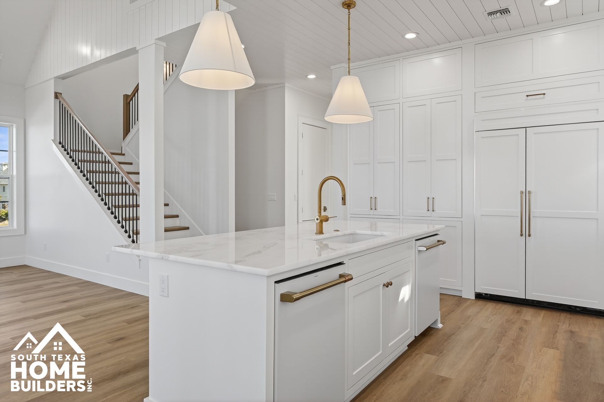 Bright white modern kitchen with gold fixtures, pendant lights, and wood floors