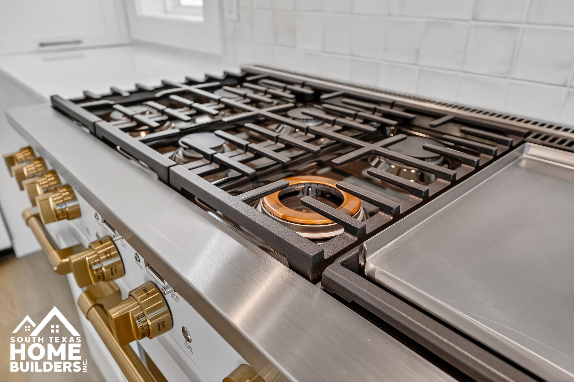 Modern stainless steel gas range with multiple burners and gold knobs in a tiled kitchen