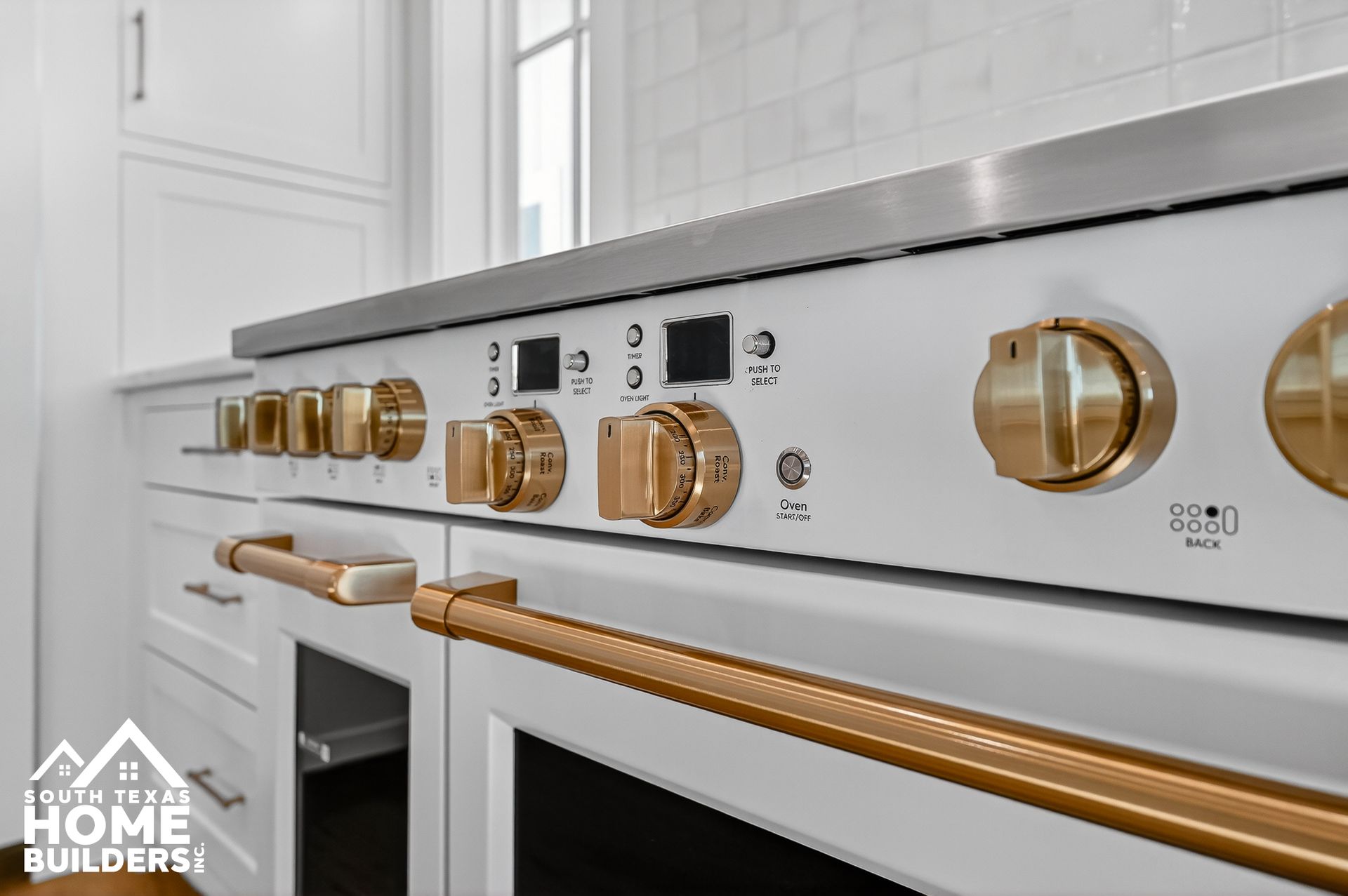 Close-up of a white stainless-steel stove with gold knobs and trim in a bright kitchen