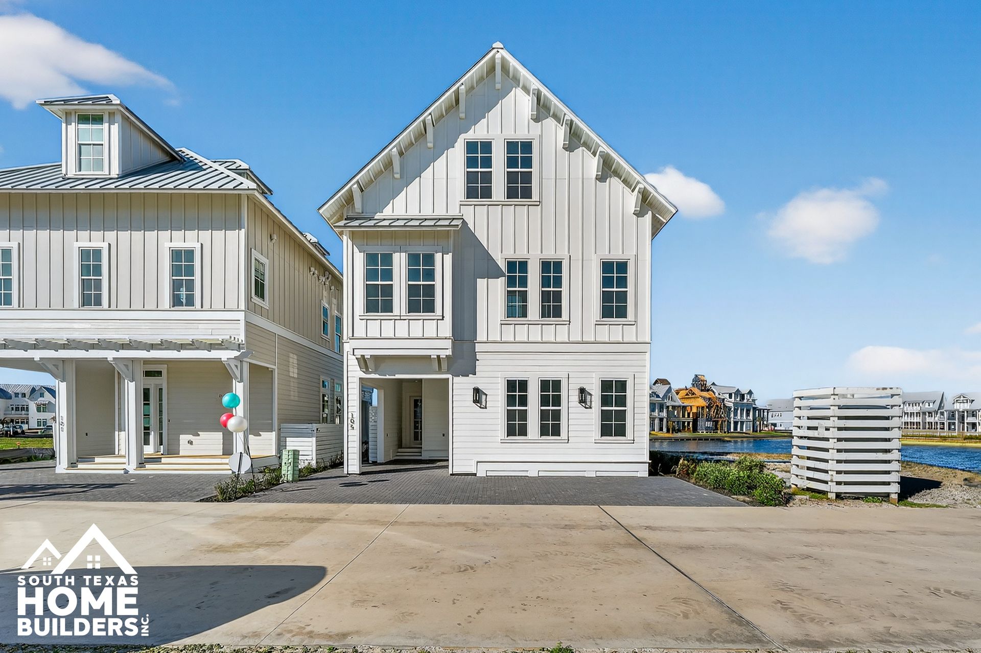 Two white coastal-style homes by a harbor under a blue sky, with a HOME BUILDERS logo in the corner