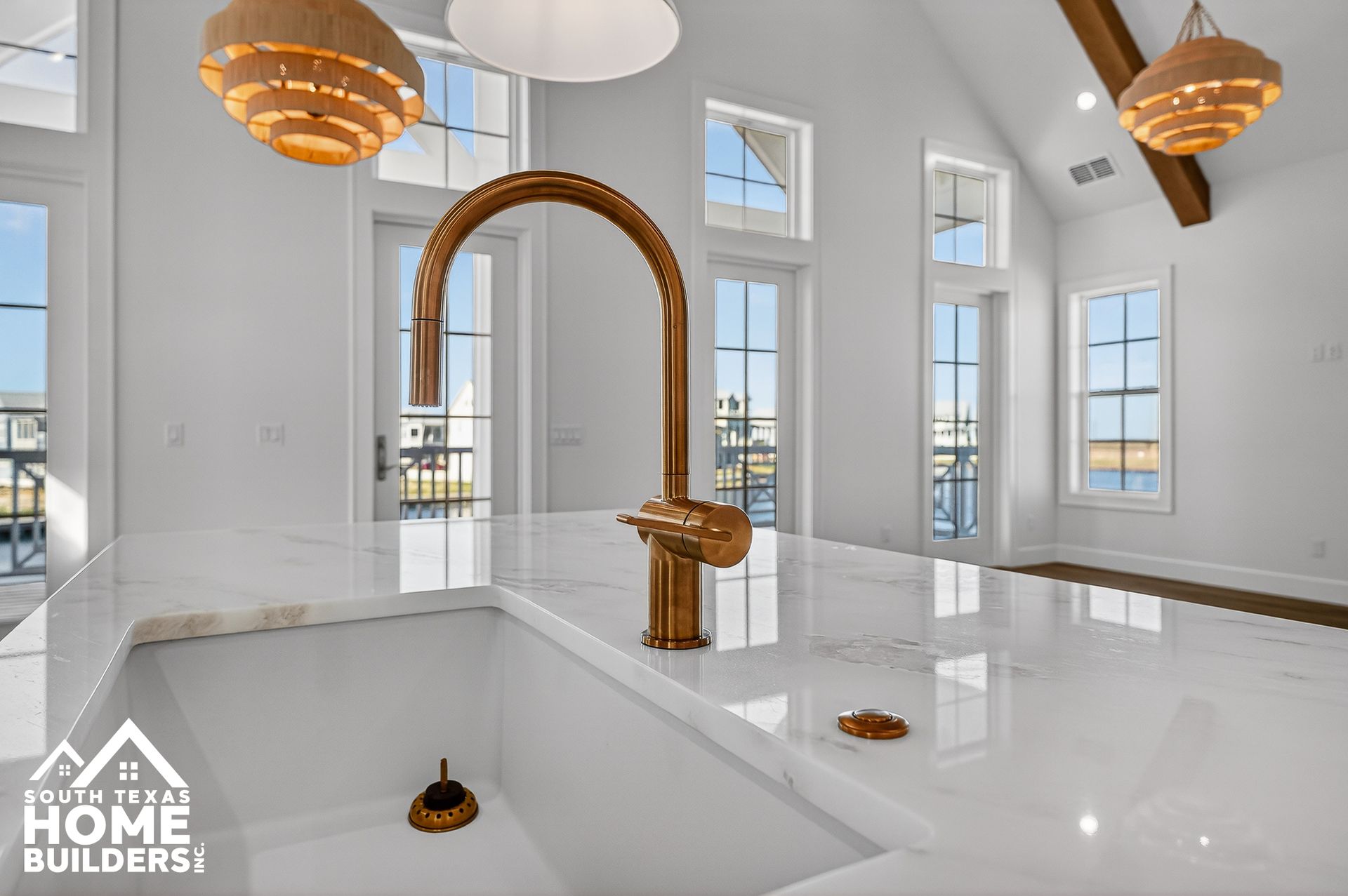 Bright luxury bathroom with white marble floors, arched mirror, gold fixtures, and large windows.