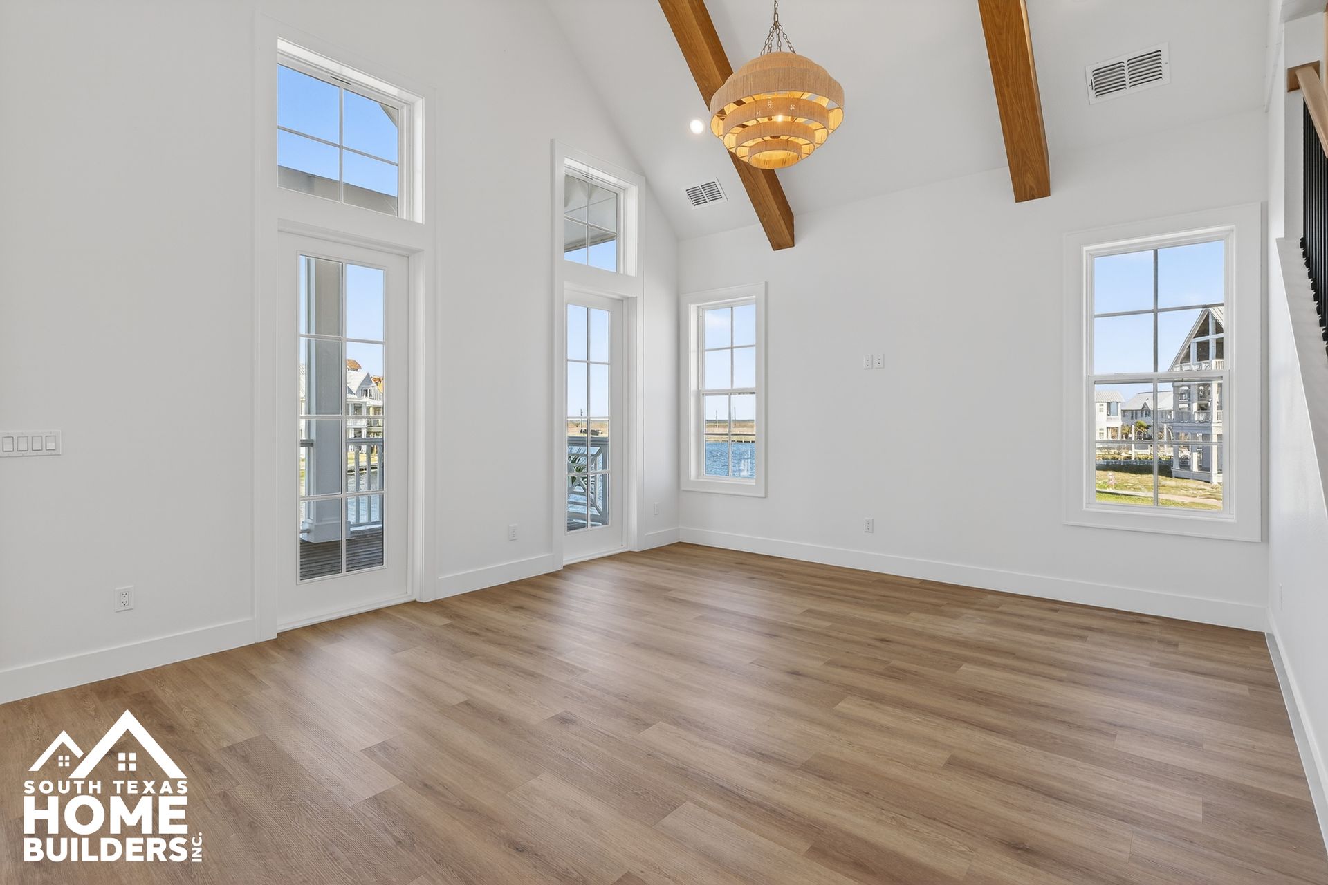 Bright empty living room with high windows, wood floors, exposed beams, and a modern ceiling fan
