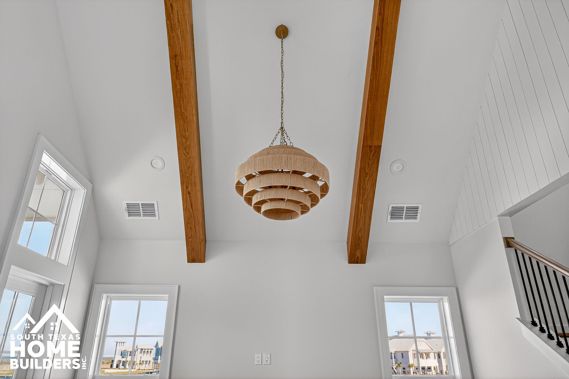 White vaulted ceiling with wood beams, a hanging modern chandelier, and bright windows in a home interior