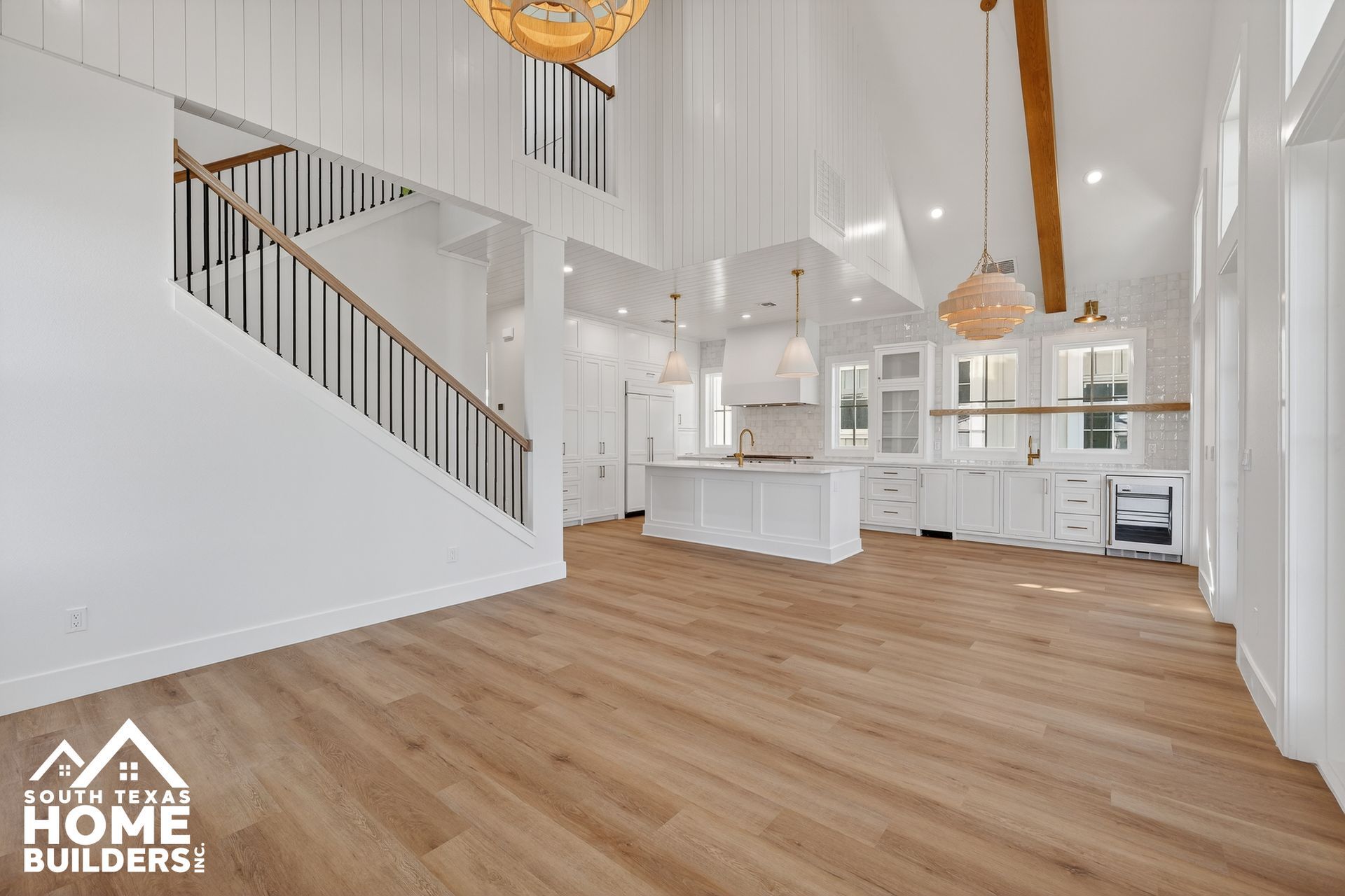 Bright white open-concept living room with wood floors, staircase, and kitchen island behind glass doors