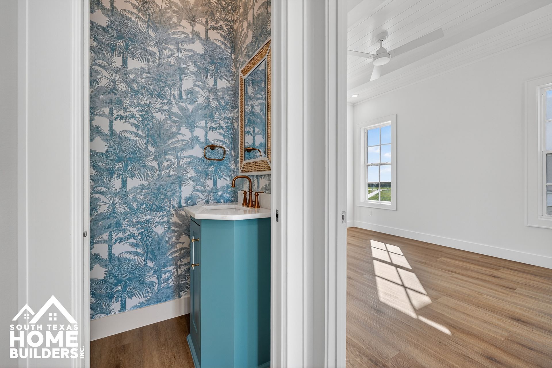 Bright hallway with blue patterned wallpaper and a small sink opening into a white room with wood floors.