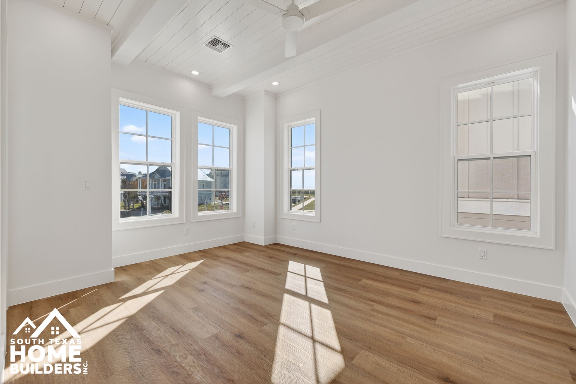 Bright empty room with white walls, tall windows, and sunlit hardwood floors