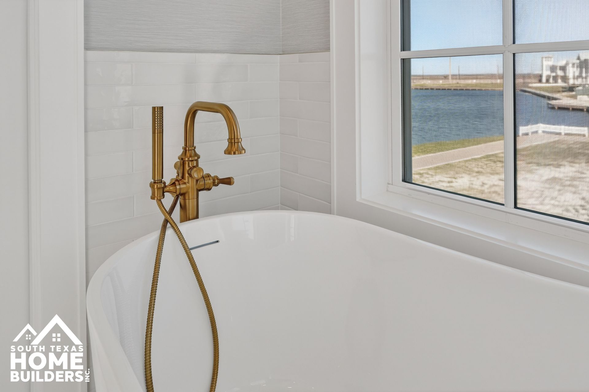 Modern bathroom with gold faucet, white tub, and ocean-view window