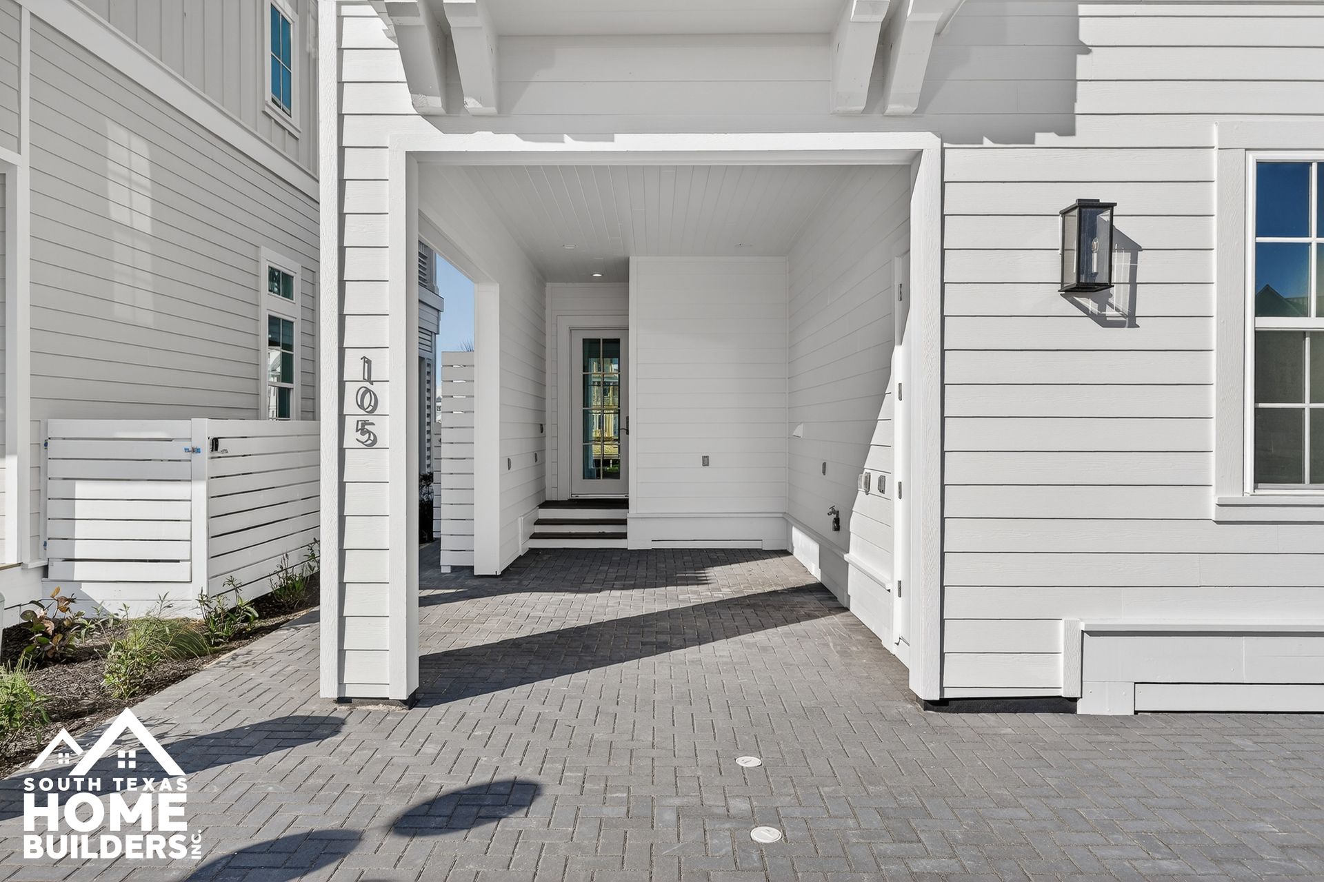 Covered white house entryway with paver walkway and a wall lantern