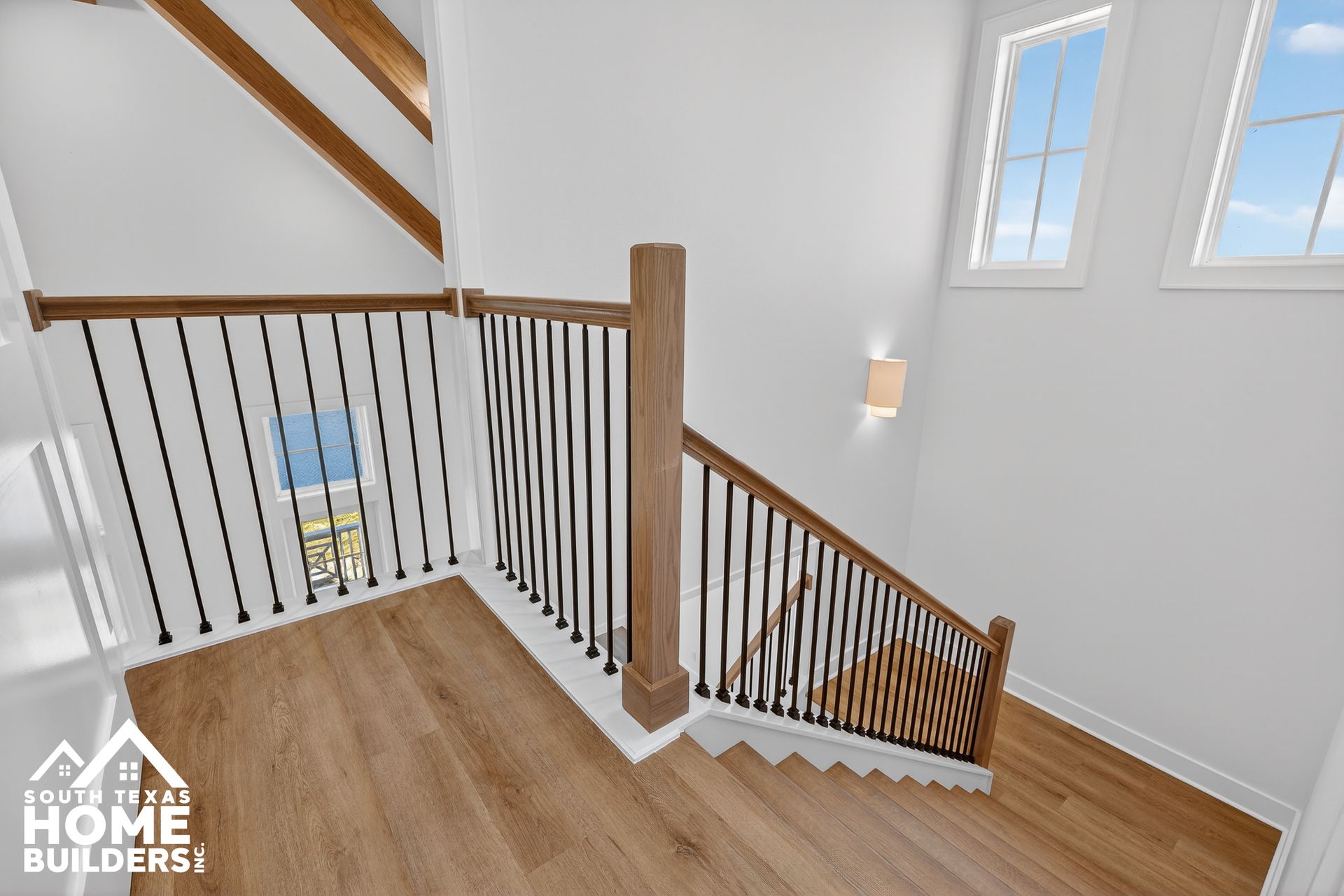 Stair landing with wood floors, white walls, and black metal railing in a bright home interior