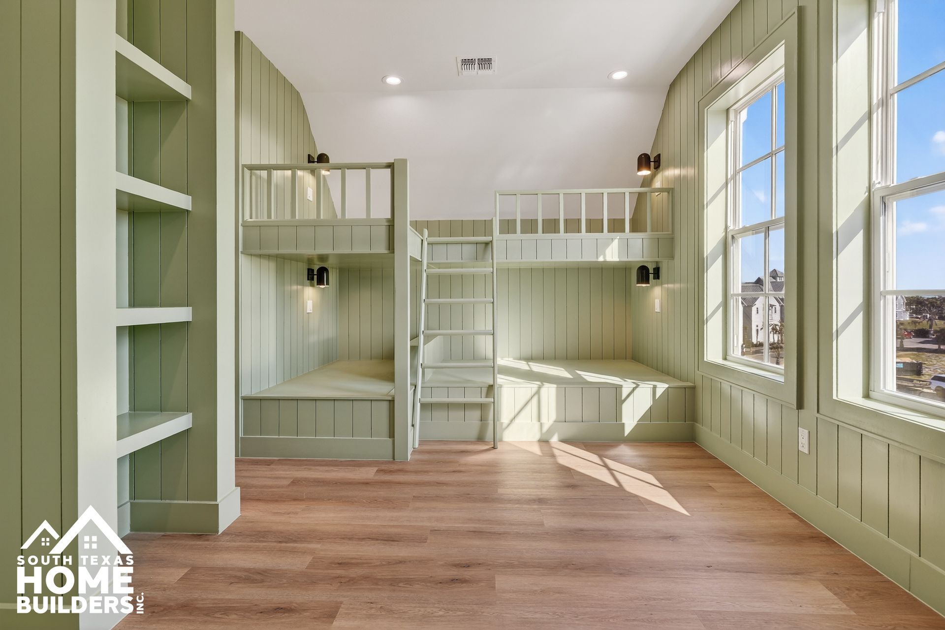Light green built-in bunk room with ladder, shelving, and wood floors in bright natural light