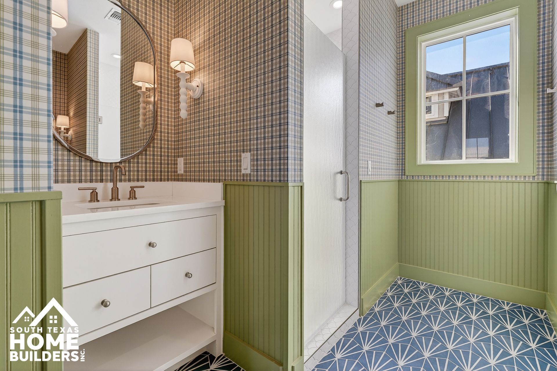 Bright bathroom with white vanity, round mirror, glass shower, green paneling, and blue patterned tile floor