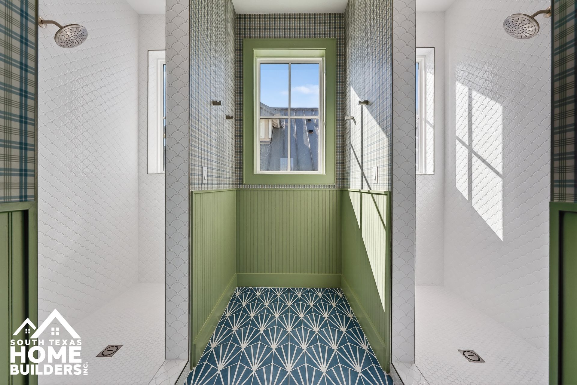 Narrow green and white tiled bathroom with blue patterned floor and a small window.