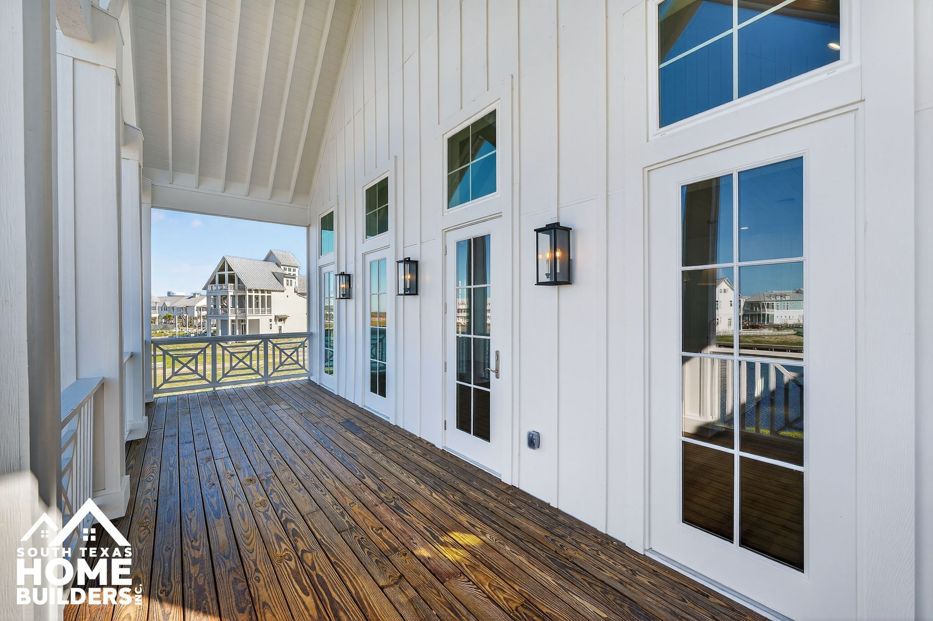 White porch with wood floor, French doors, and railings overlooking a waterfront neighborhood