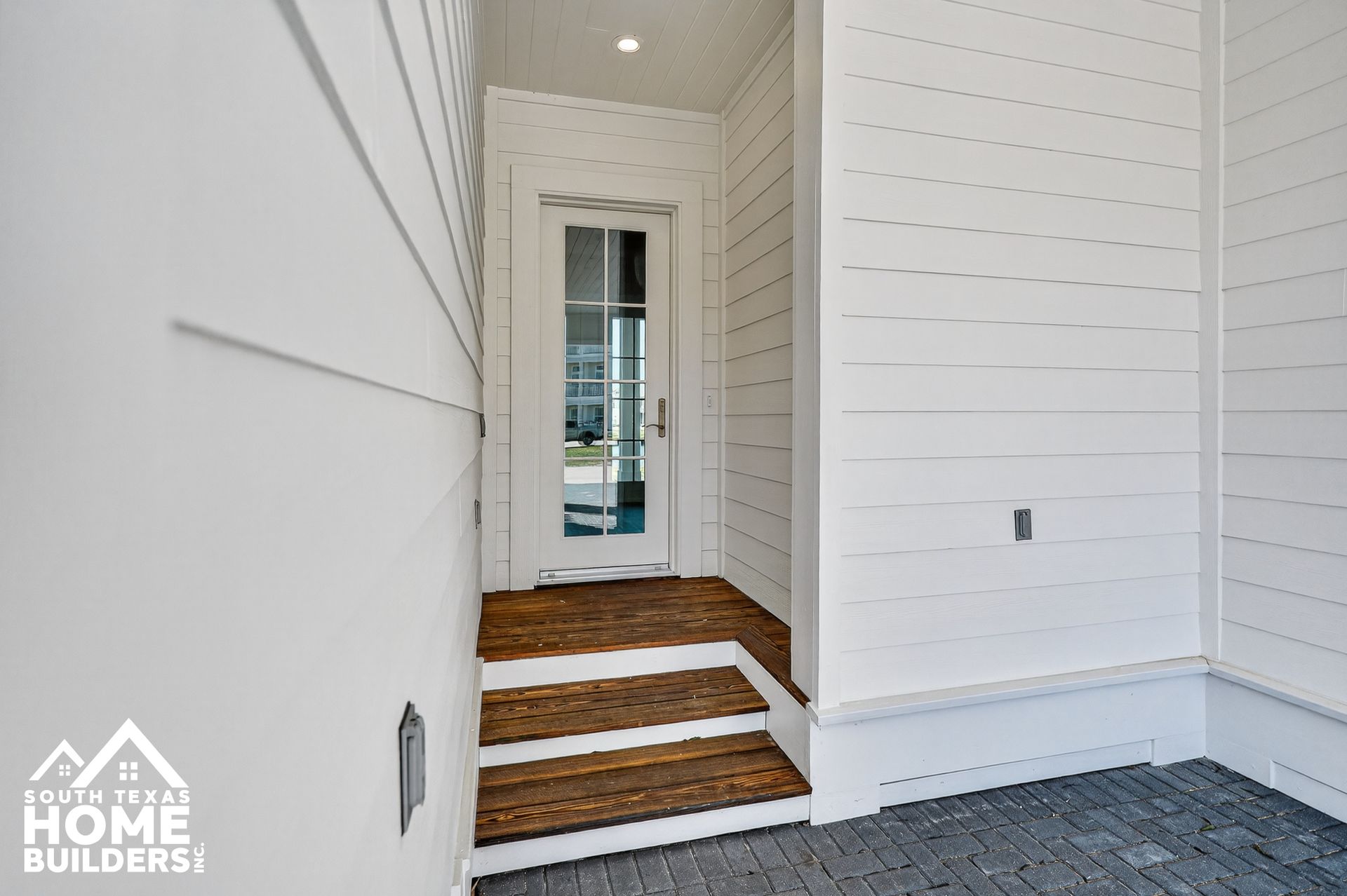Front porch entry with white siding, dark steps, and a glass front door leading inside