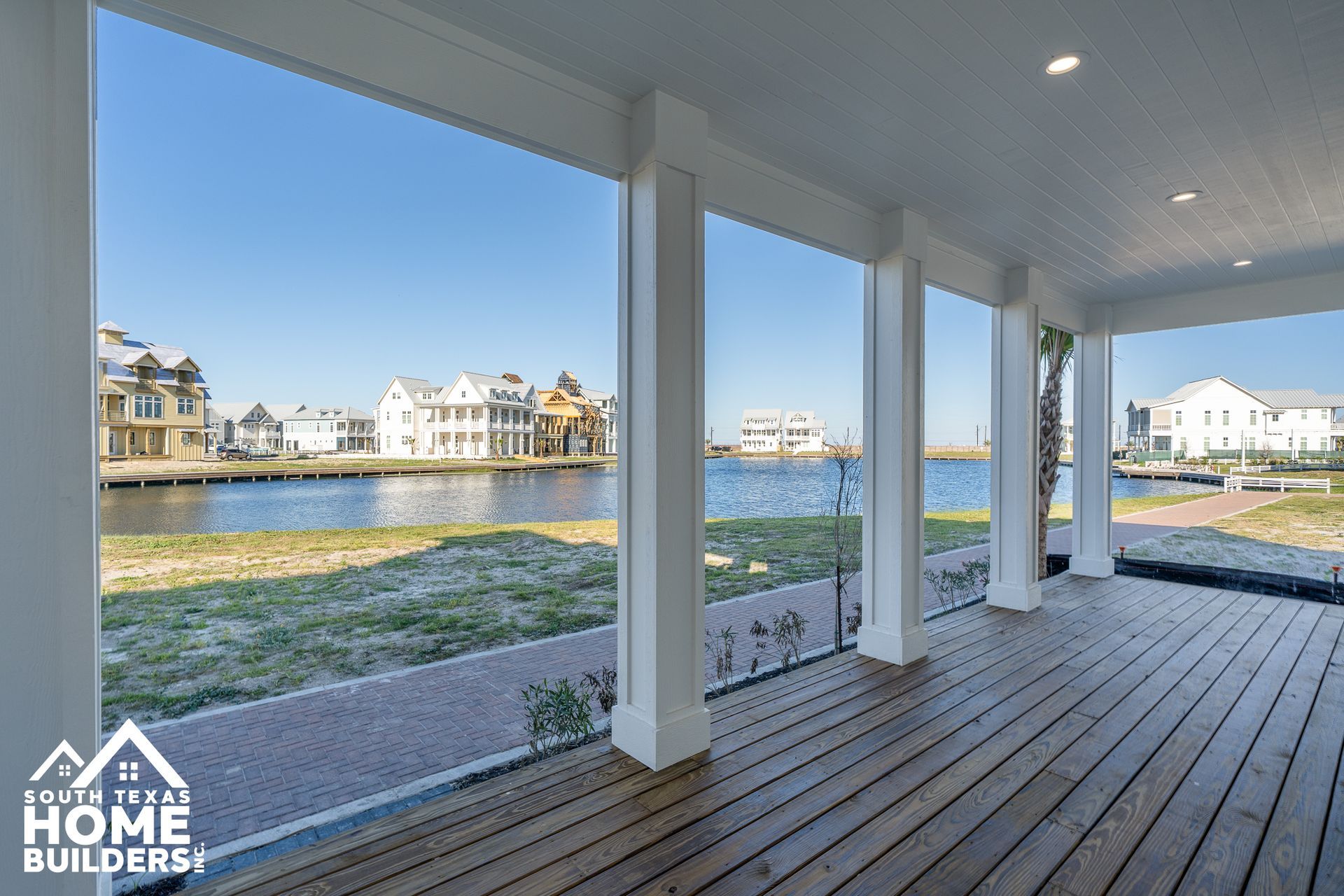 Covered porch overlooking a waterfront neighborhood with white homes and a grassy shore